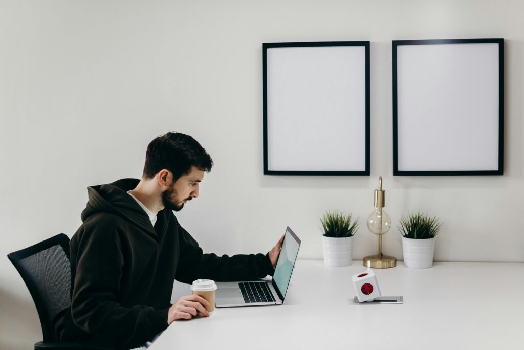 Young man in a hoodie works on a laptop in a modern, minimalist home office setup.